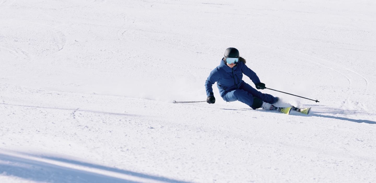 Skifahrer in einem blauen Anzug fährt an einem sonnigen Wintertag einen schneebedeckten Berghang hinunter.
